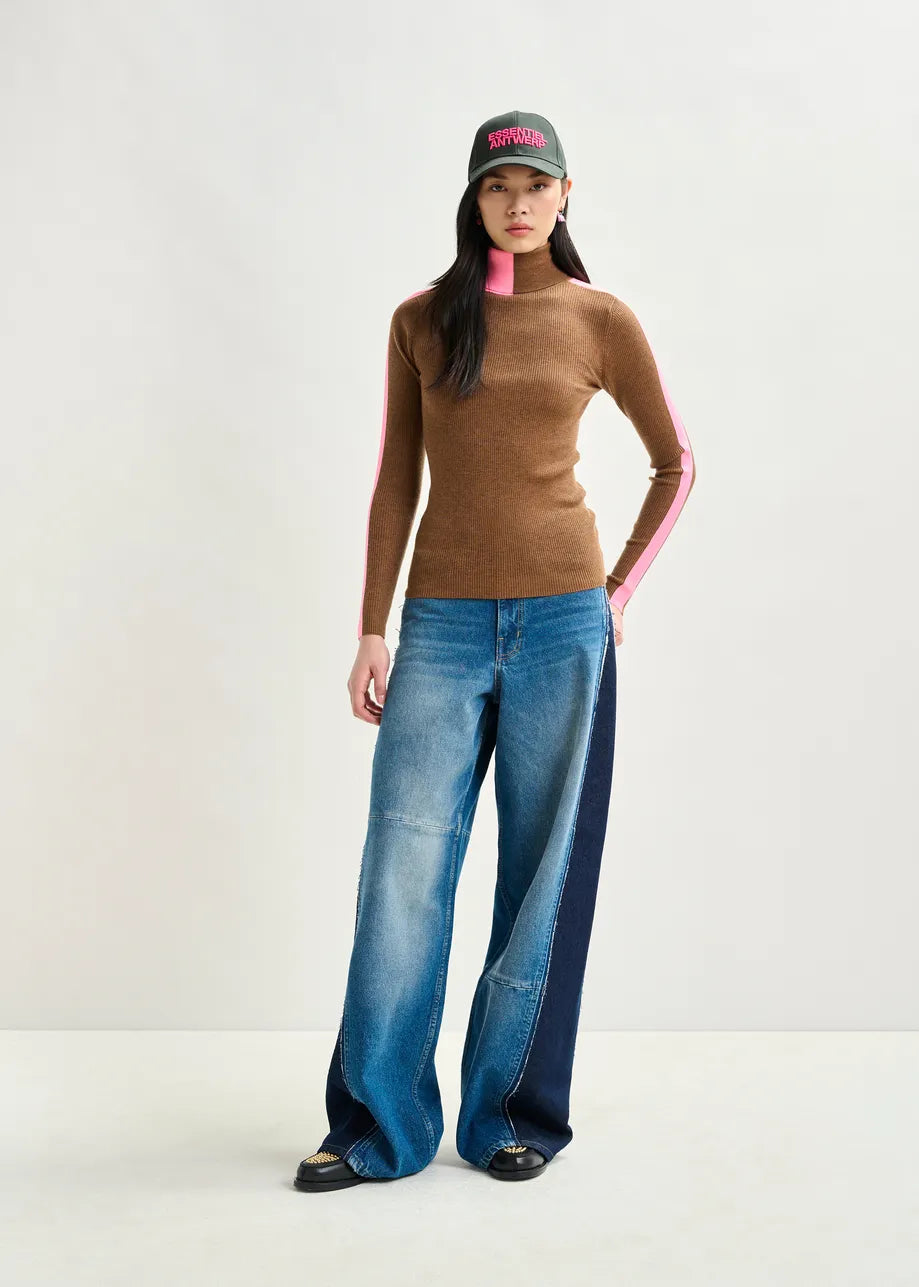 Person wearing a brown top with pink accents and blue jeans on a white background