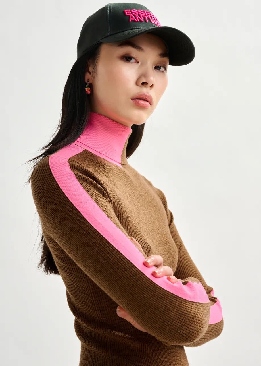 Person wearing a brown sweater with pink accents and a black cap on a white background