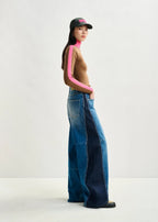 Person wearing a brown sweater with pink accents and blue jeans on a white background
