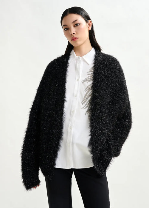Woman wearing a black fuzzy cardigan over a white shirt on a white background