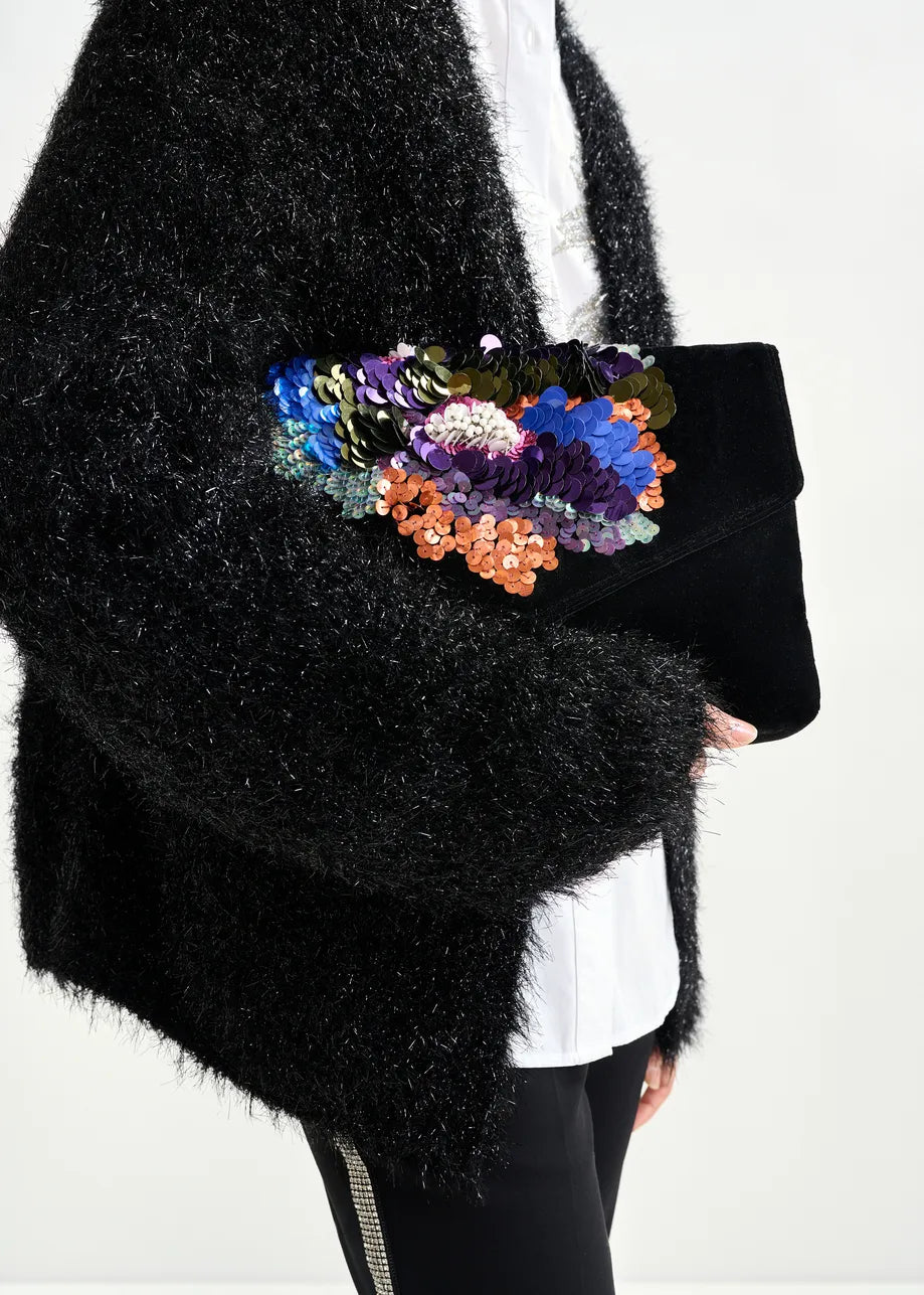 Person wearing a black textured coat with a colorful floral clutch bag on a white background