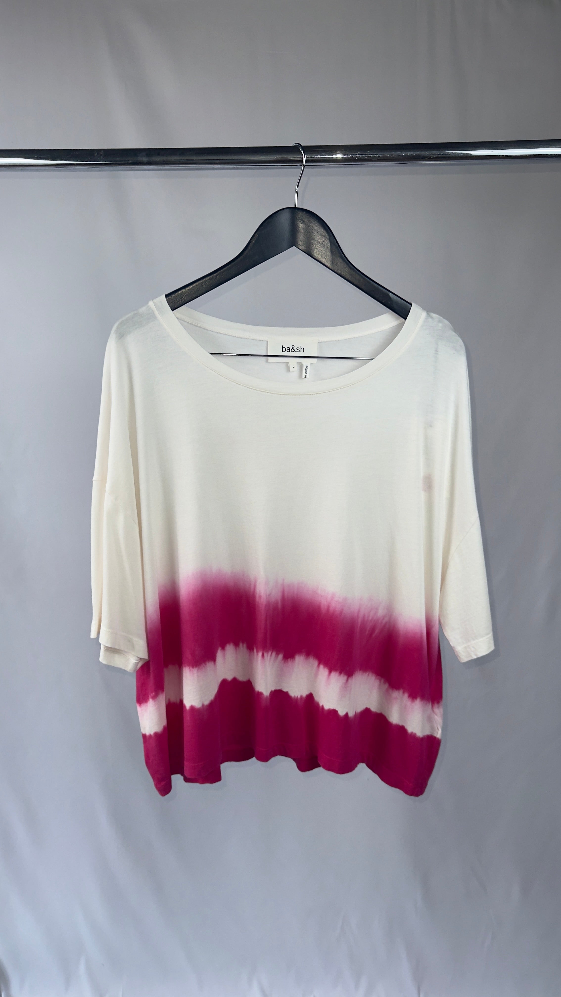 White and magenta tie-dye shirt on a hanger against a plain background