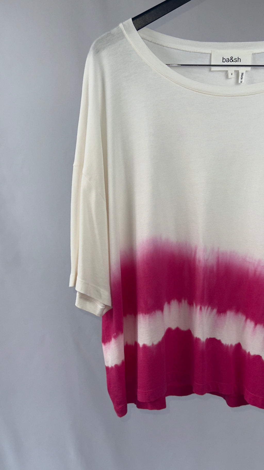 White and pink tie-dye shirt on a hanger against a gray background