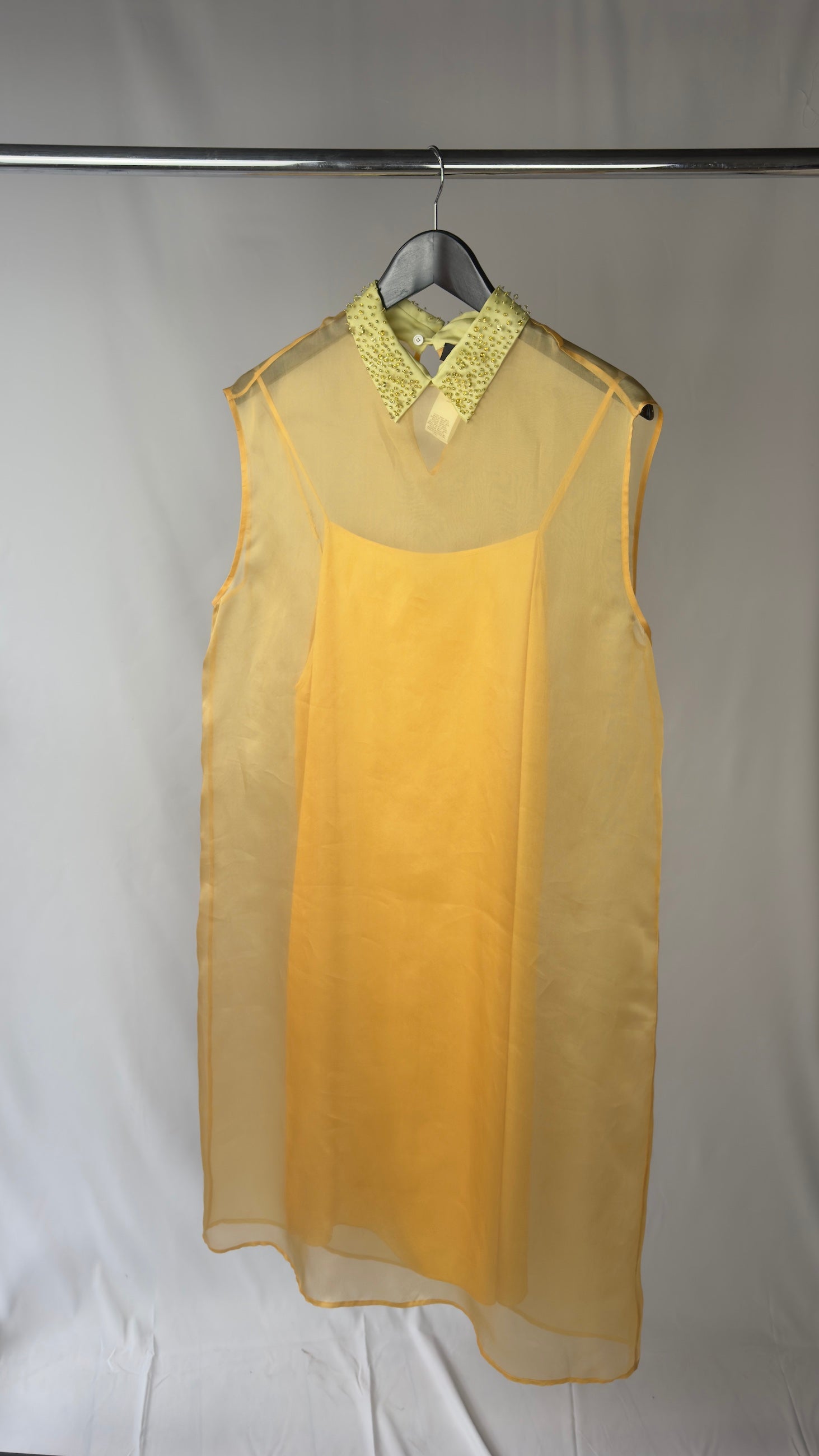 Yellow sheer top with green lace collar on a hanger against a gray background