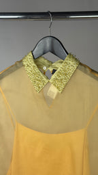 Sheer beige blouse with green sequin collar on a hanger against a gray background