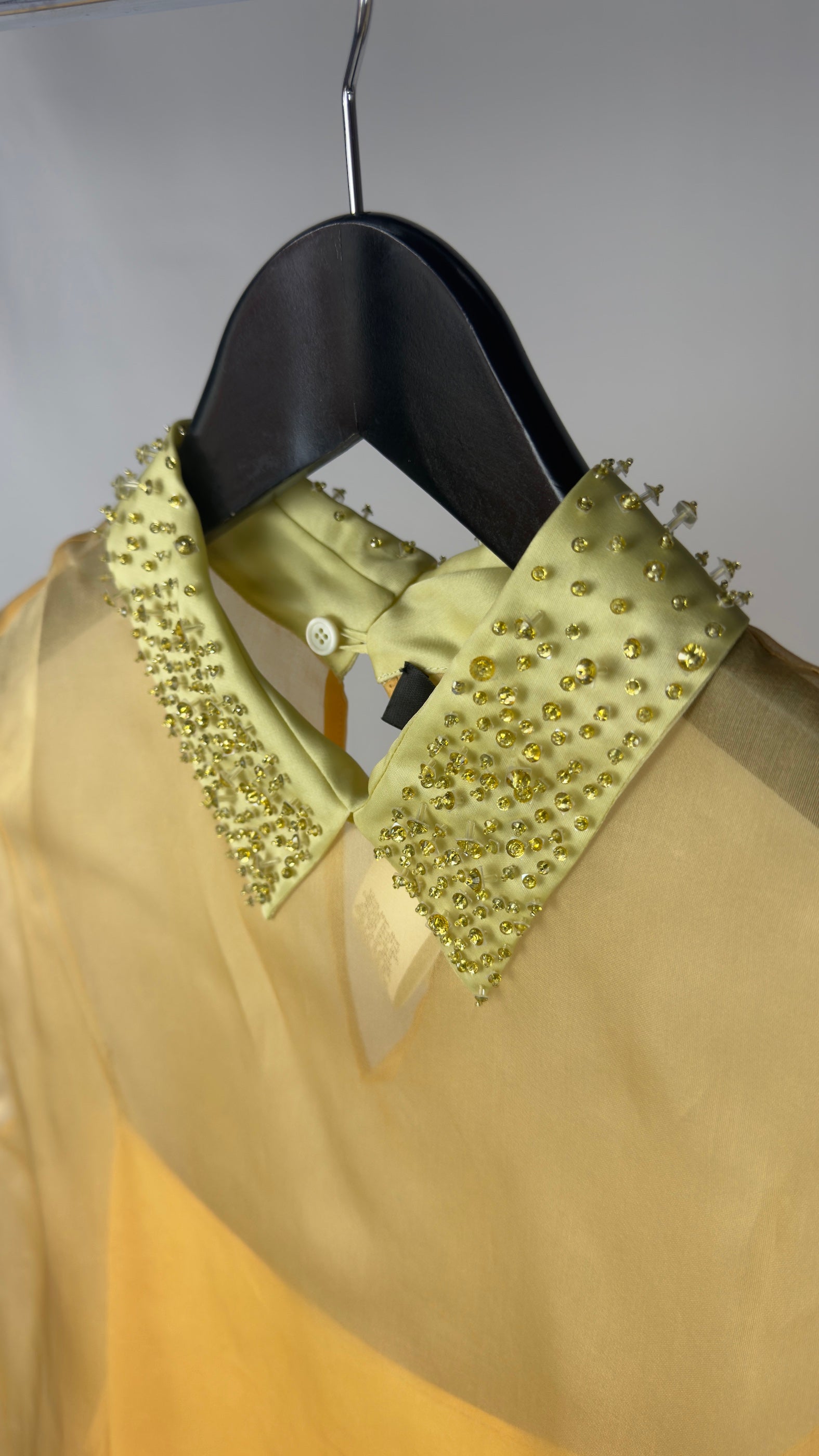 Gold blouse with studded collar on a hanger against a neutral background
