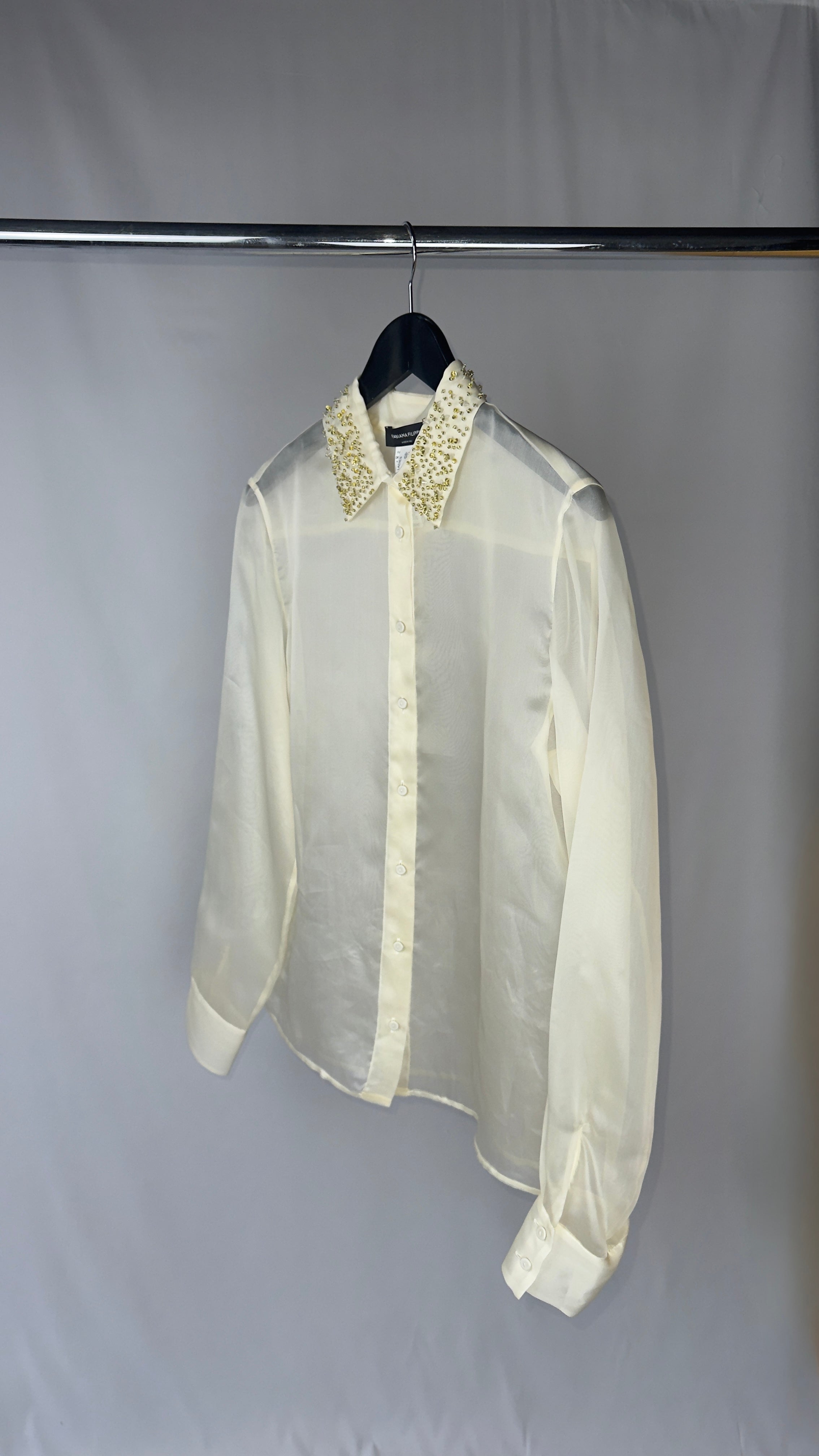 White sheer blouse with embellished collar on a hanger against a gray background