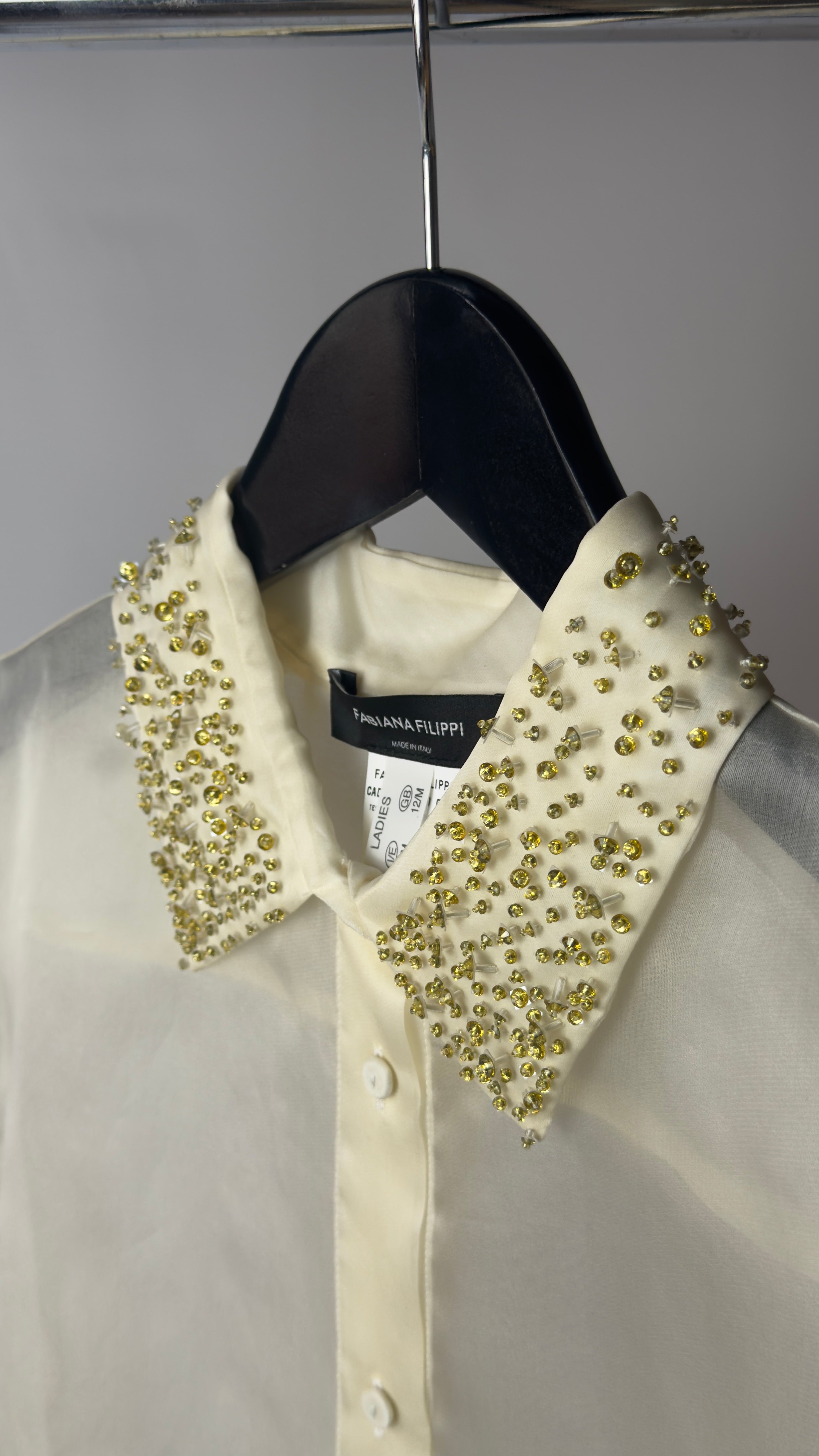 White shirt with a decorative green collar on a hanger against a gray background