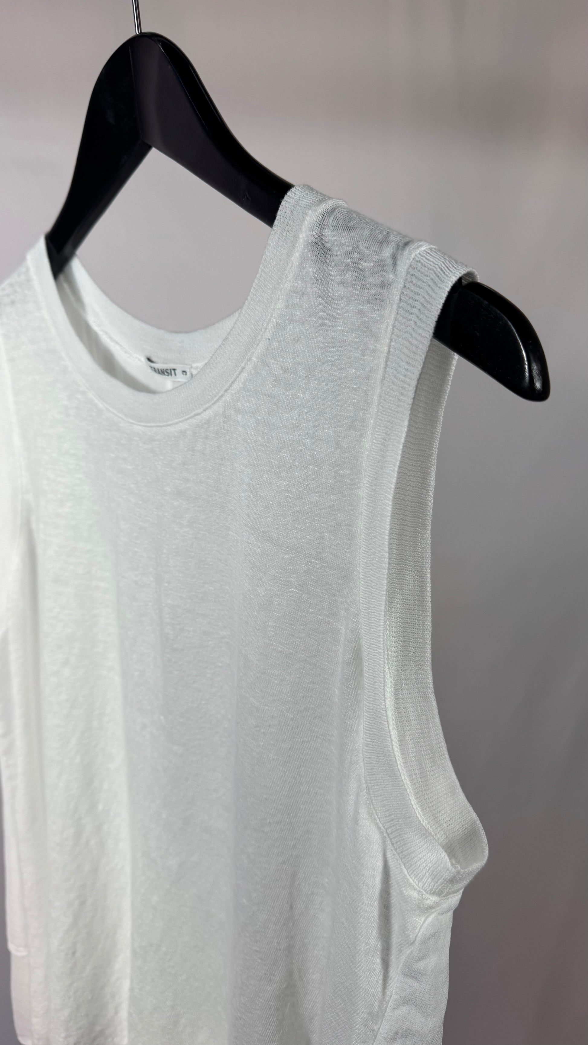 White sleeveless shirt on a black hanger against a plain background