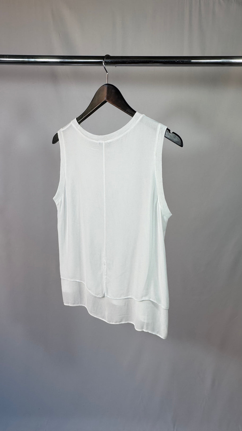 White sleeveless top on a hanger against a plain background