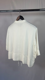 White textured sweater on a hanger against a plain background