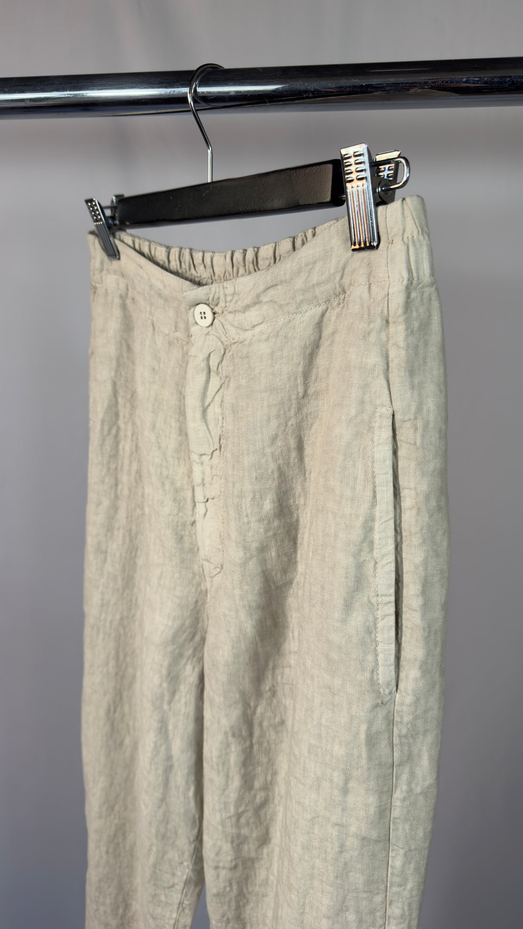 Beige pants hanging on a rack against a gray background