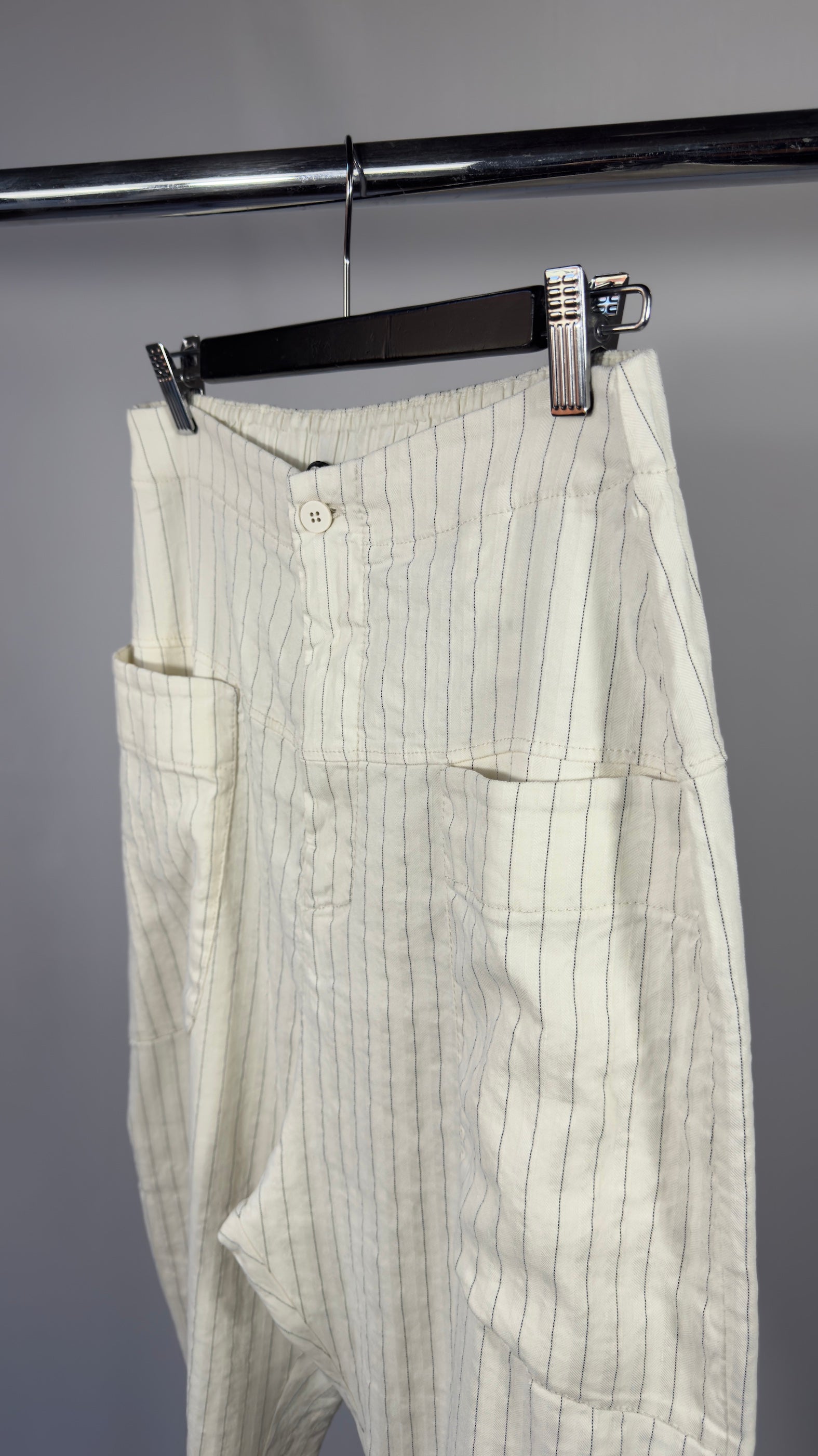 White pinstripe pants hanging on a rack against a gray background
