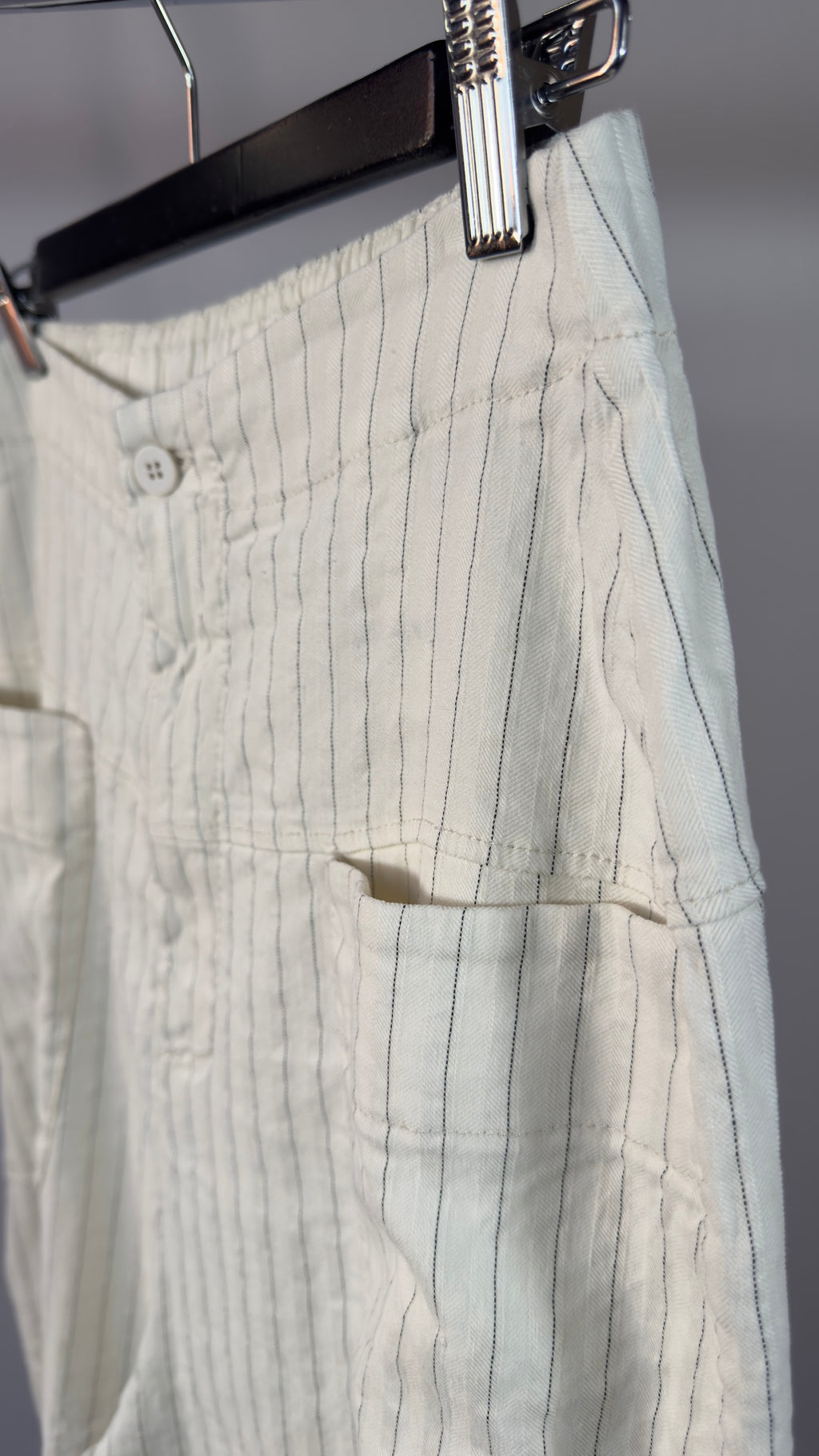 Light-colored pants with vertical stripes hanging on a hanger against a neutral background