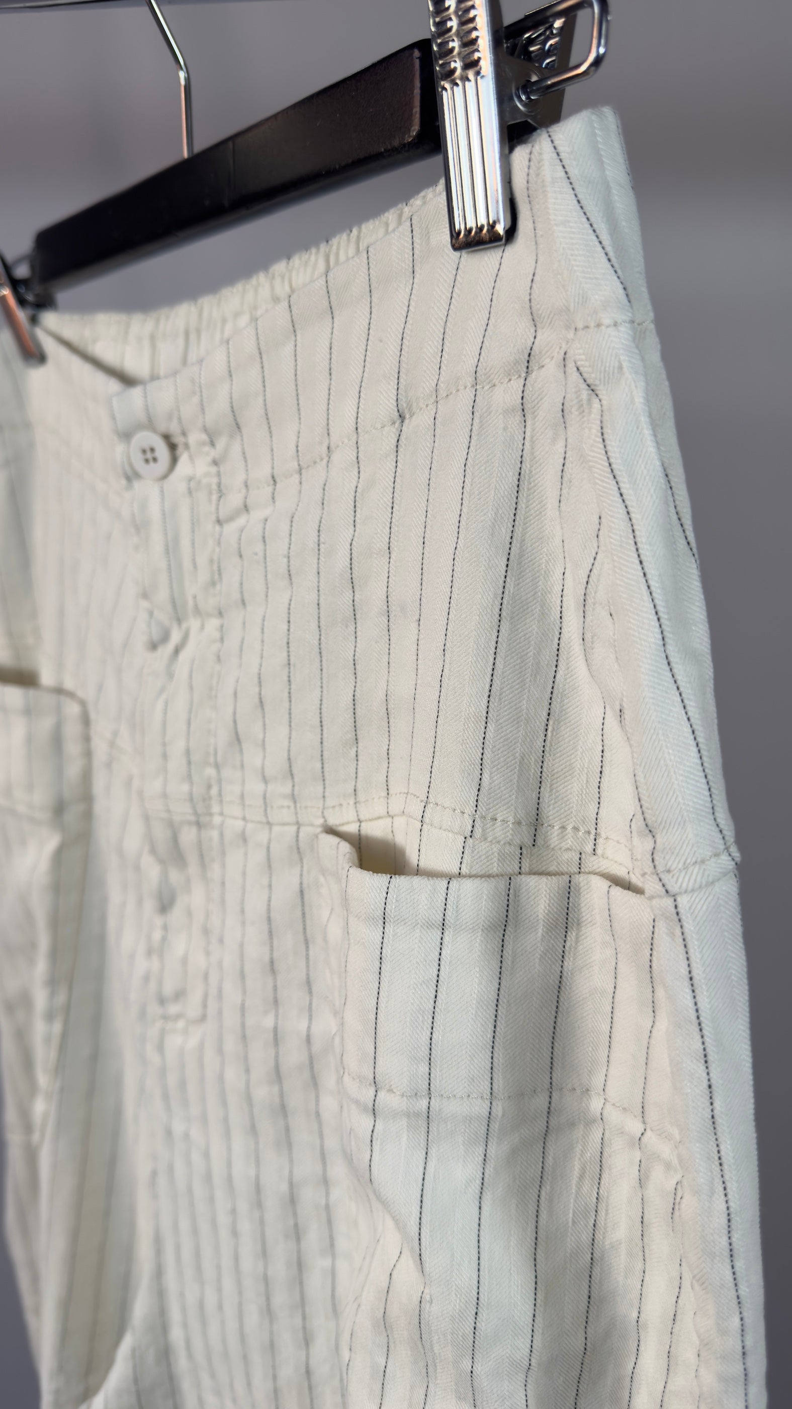 Light-colored pants with vertical stripes hanging on a hanger against a neutral background