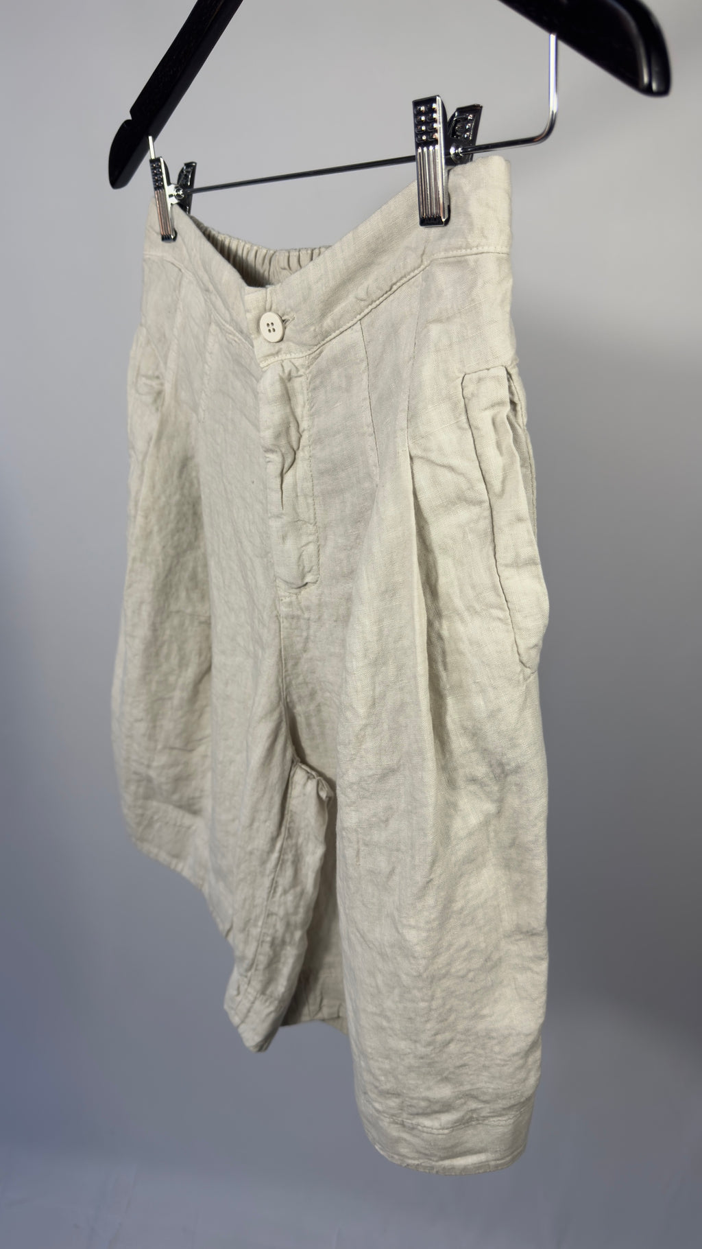 Light-colored pants hanging on a hanger against a gray background