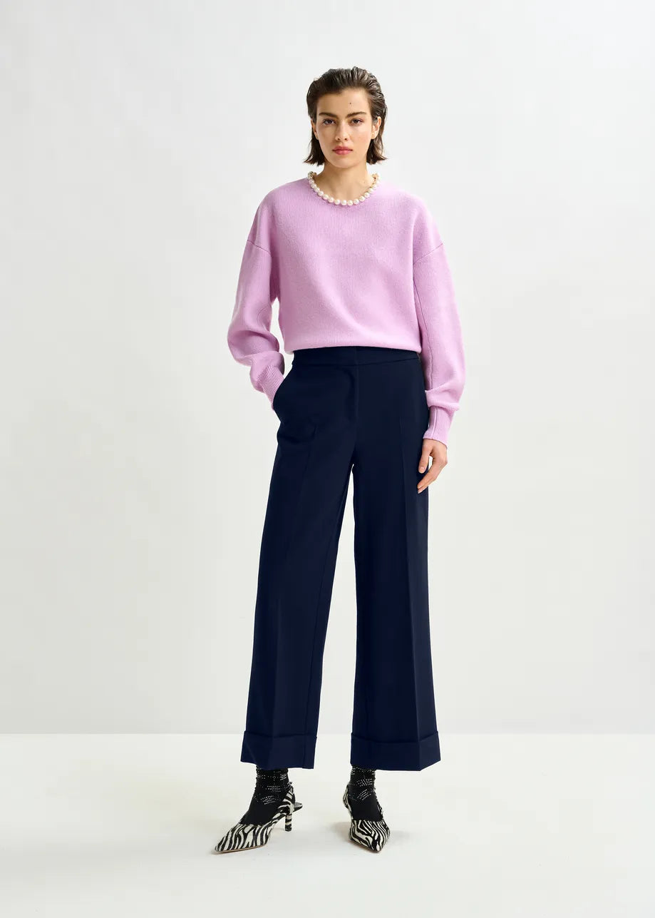 Person wearing a pink sweater and navy pants on a white background