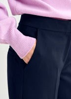 Person wearing a pink sweater and dark pants with a plain background