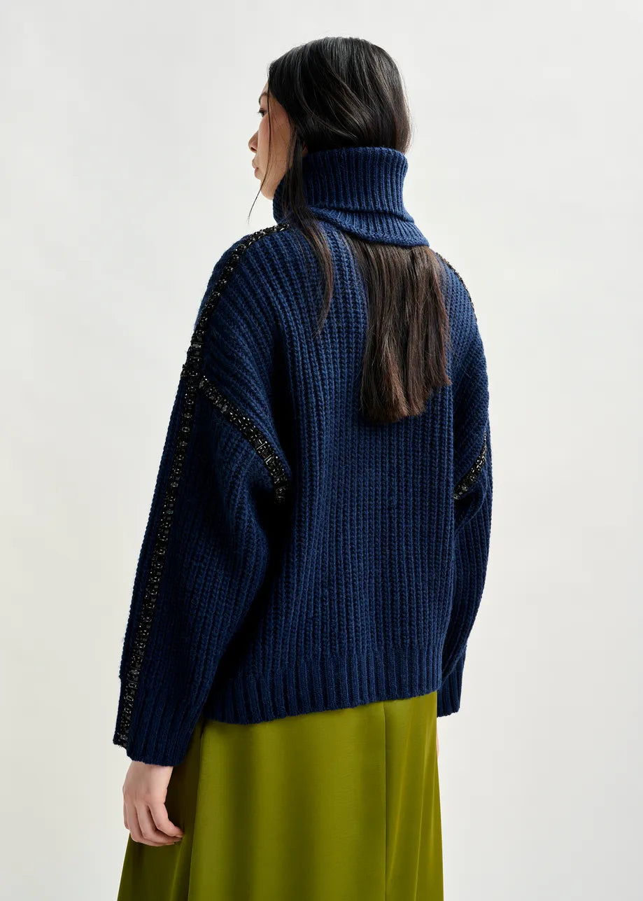 Person wearing a blue knitted sweater with decorative elements on a white background