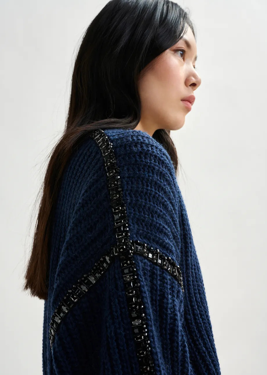 Woman wearing a blue knitted garment with decorative elements on a plain background
