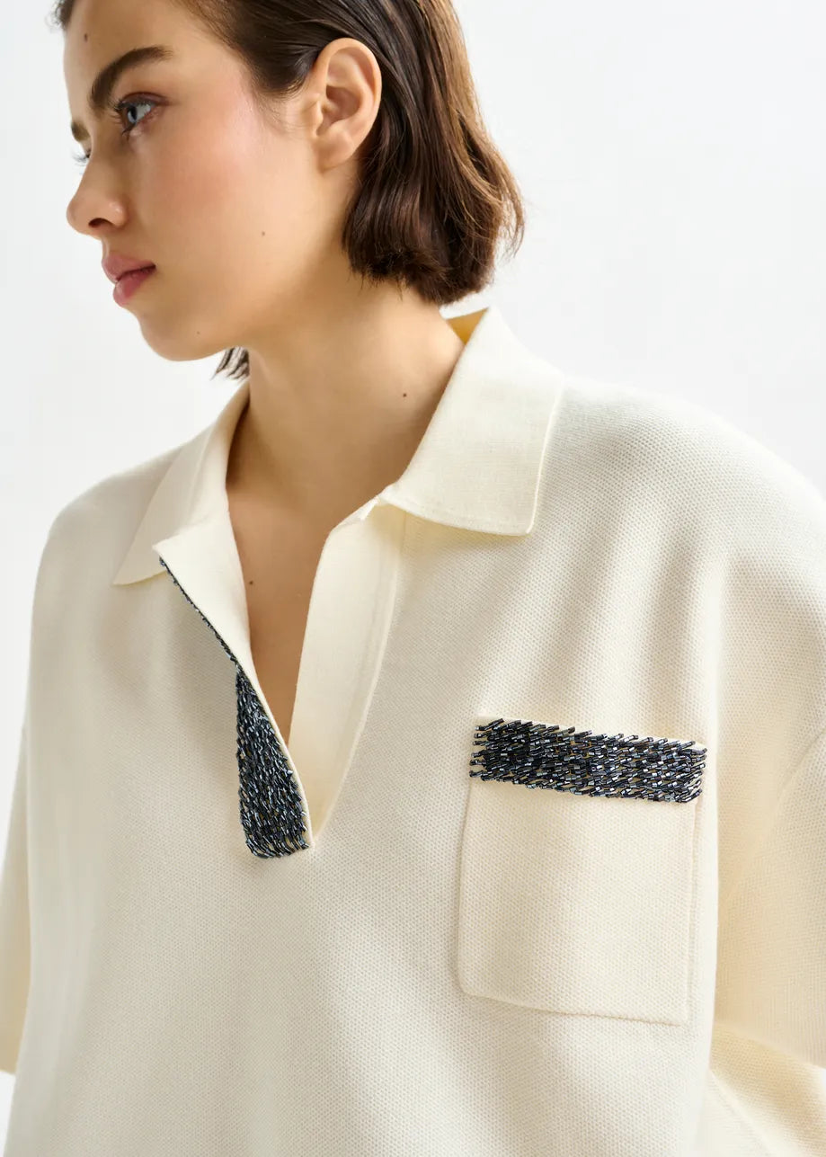 Woman wearing a cream-colored blouse with decorative black trim on a white background