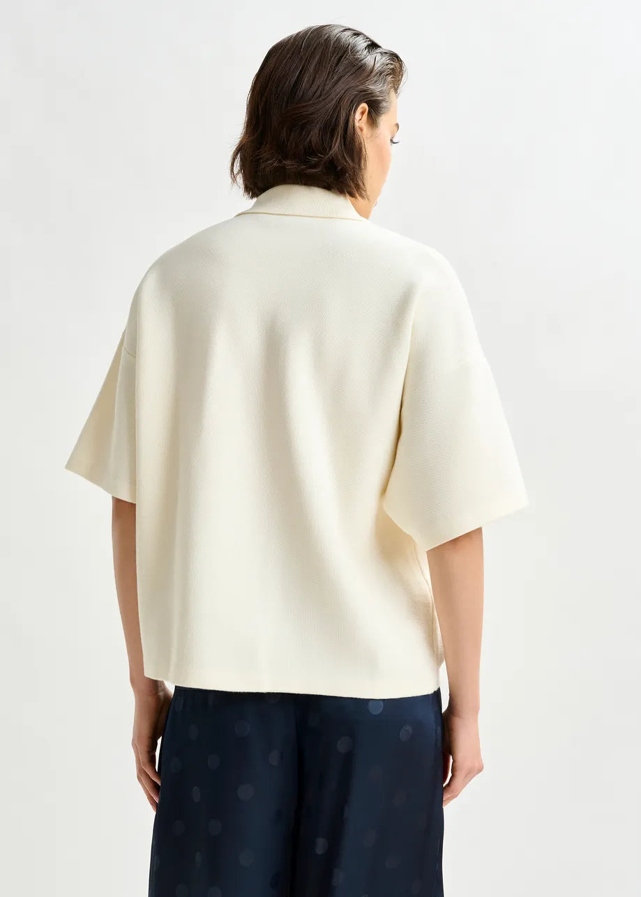 Person wearing a cream-colored shirt with navy pants on a white background