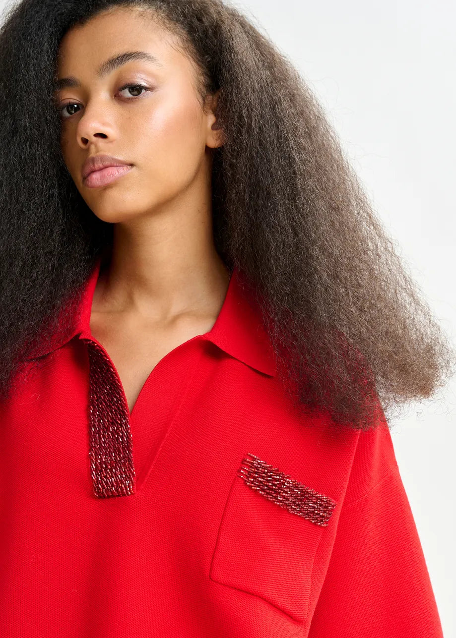 Woman wearing a red shirt with embellished collar and pocket on a white background