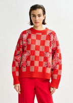 Person wearing a red checkered sweater with sequin details on a white background