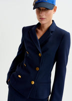 Person wearing a navy blue double-breasted jacket with gold buttons and a matching cap on a light gray background.