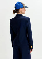 Person wearing a navy blazer and pants with a blue cap on a light gray background