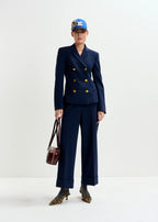 Person wearing a navy blue suit with gold buttons, holding a brown handbag on a white background