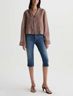 A model wearing a dusty rose textured jacket, blue cropped jeans, and black strappy heels against a plain white studio background.