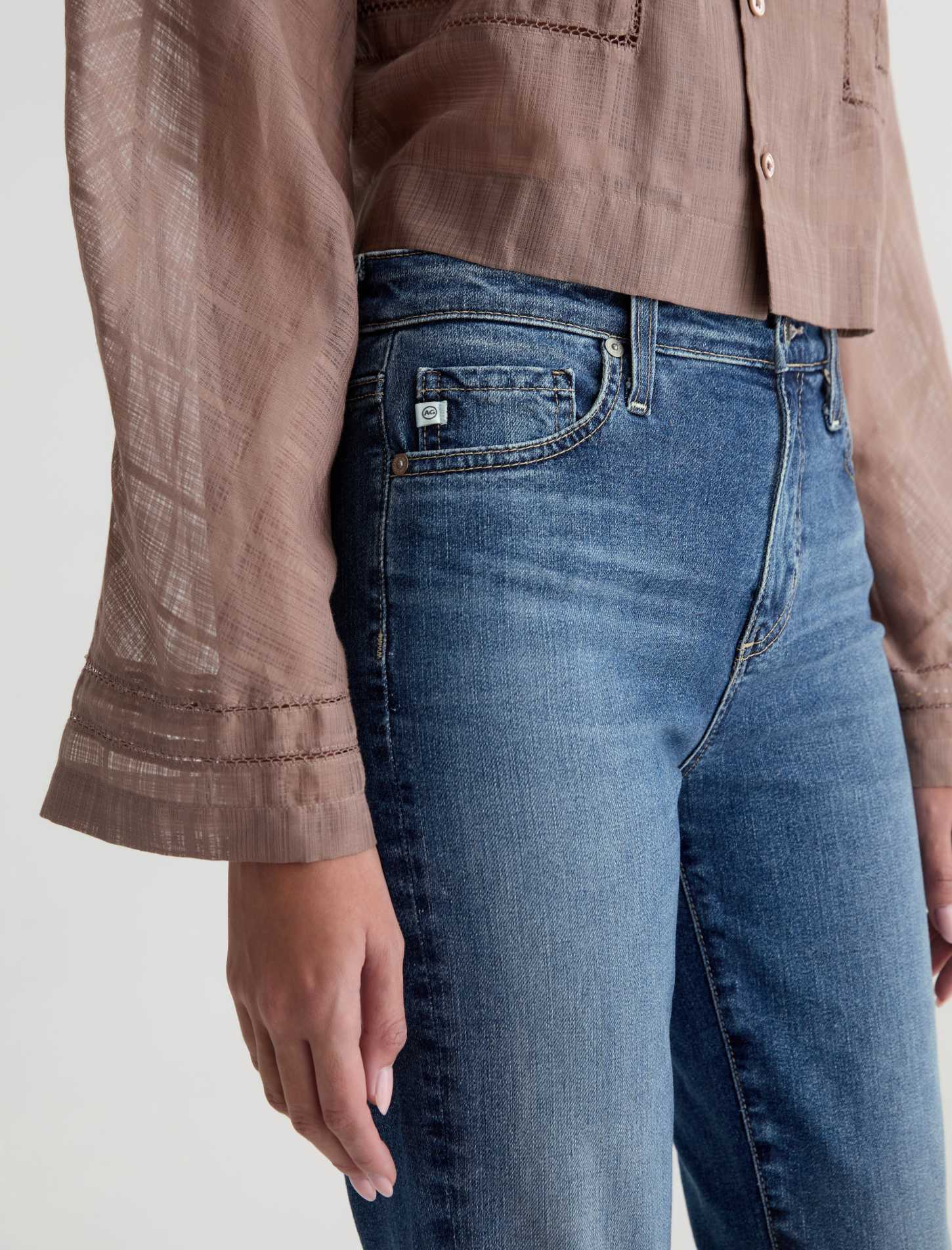 Person wearing blue jeans and a brown shirt on a plain background