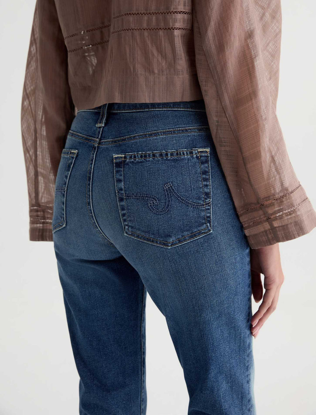 Person wearing blue jeans and a brown jacket on a white background