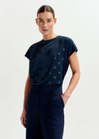 Woman wearing a navy blue dress with white polka dots on a light gray background