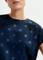 Navy blue top with light blue polka dots worn by a person on a white background