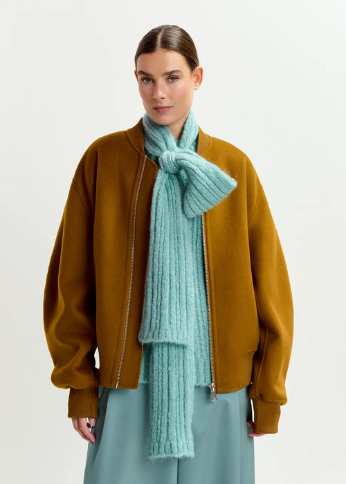 Person wearing a mustard jacket and light blue scarf on a white background