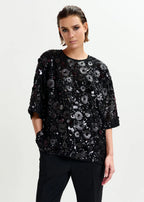 Woman wearing a black sequin top on a light gray background
