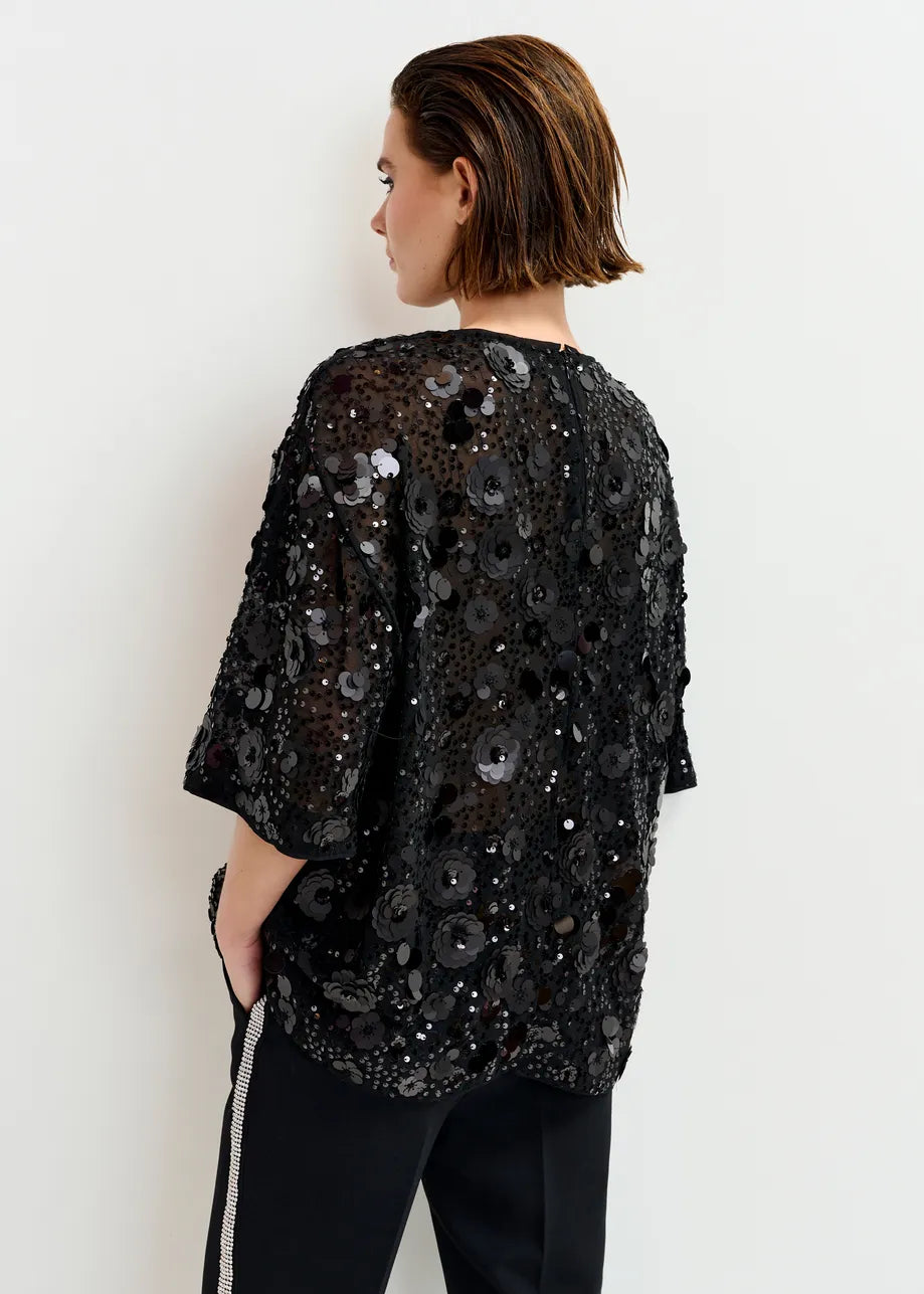 Person wearing a black sequin top against a white background