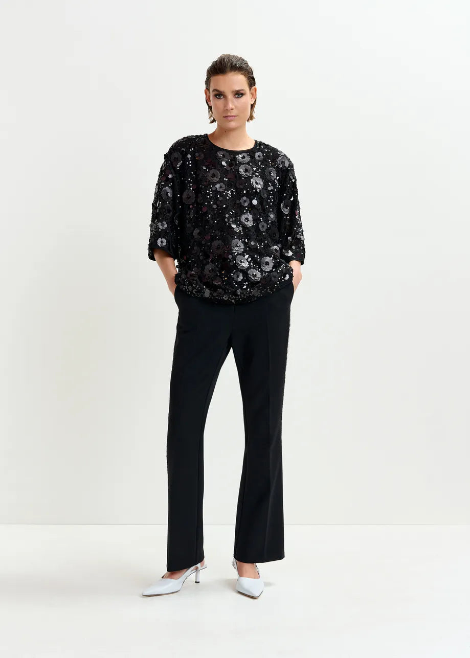 Woman wearing a black sequin top and black pants on a white background