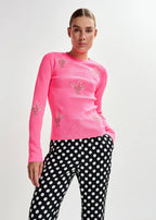 Person wearing a pink long-sleeve top with floral embellishments and black polka dot pants on a light gray background.JARDENS-CO17
