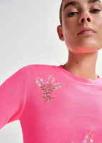 Person wearing a pink sweater with floral embroidery on a plain background