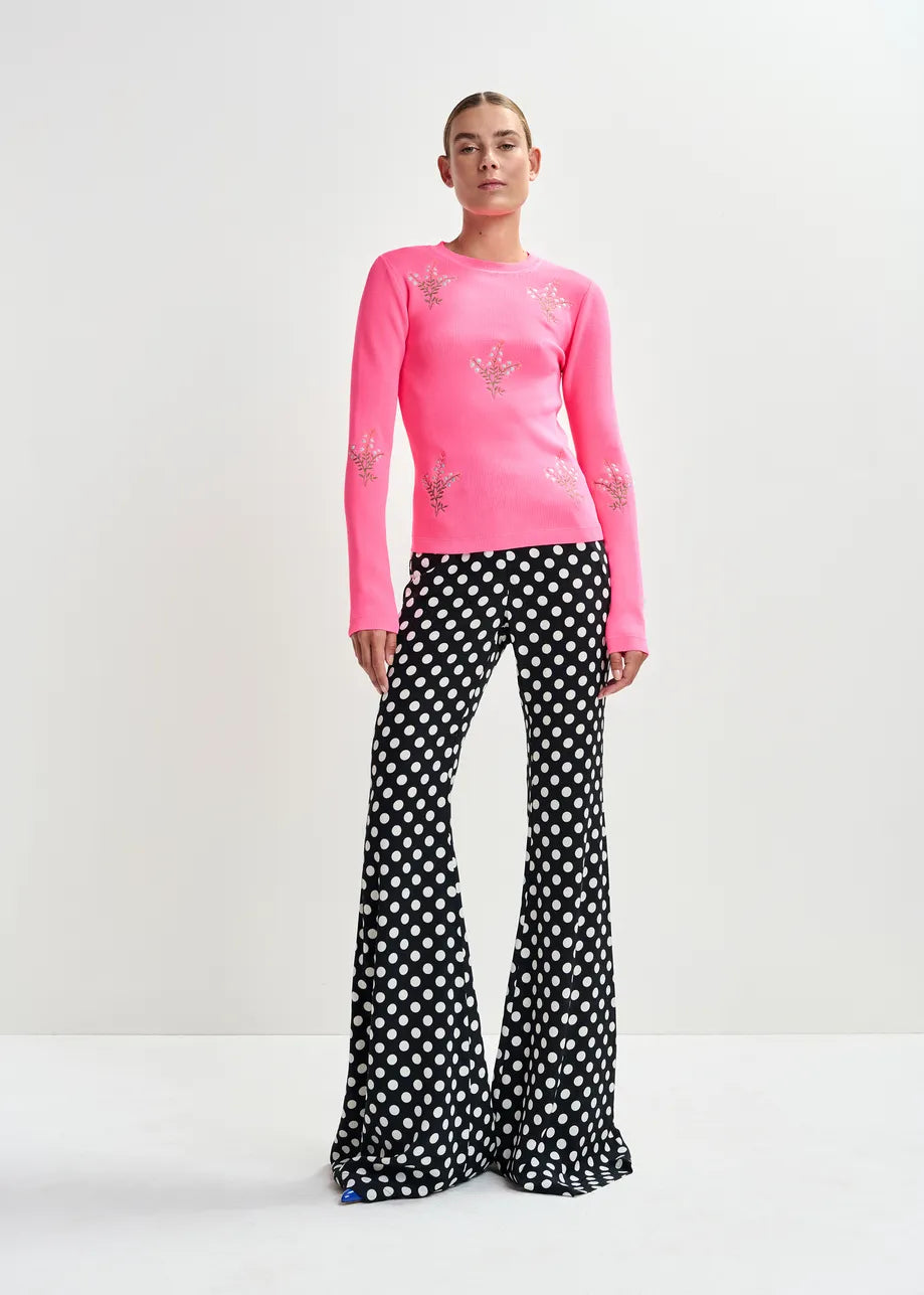 Person wearing a pink long-sleeve top with floral designs and black polka dot pants on a white background