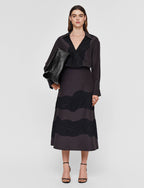 A woman standing wearing a black A-line skirt with hand-cut lace detailing and a visible side zipper.