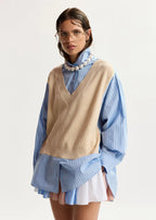Woman wearing a beige sweater over a blue shirt with a white background