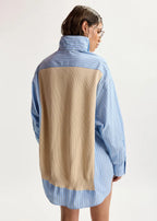 A model shown from the back wearing a color-blocked shirt with light blue and white vertical stripes on the sleeves, collar, and hem, and a large beige ribbed panel across the back.