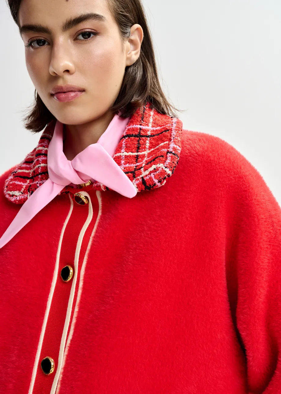 Person wearing a red coat with a plaid collar and pink bow tie on a white background