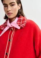 Person wearing a red coat with a plaid collar and pink bow tie on a white background