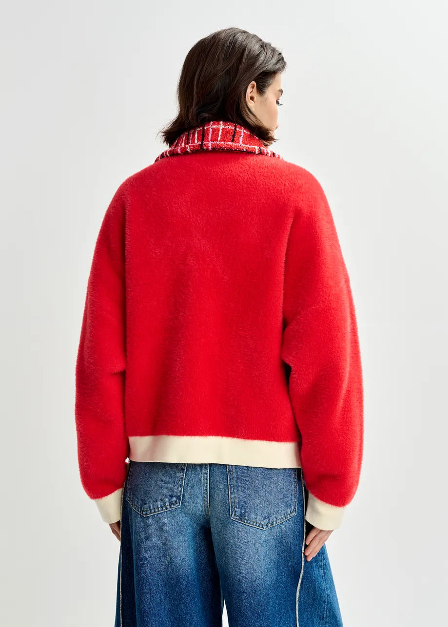 Person wearing a red sweater with a plaid collar on a light gray background