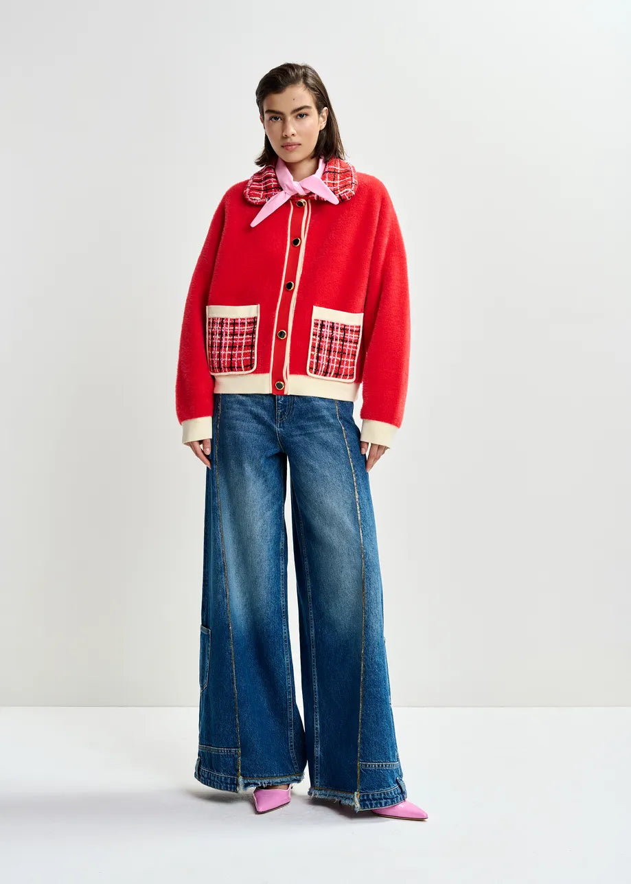 Person wearing a red jacket with plaid accents and blue jeans on a white background